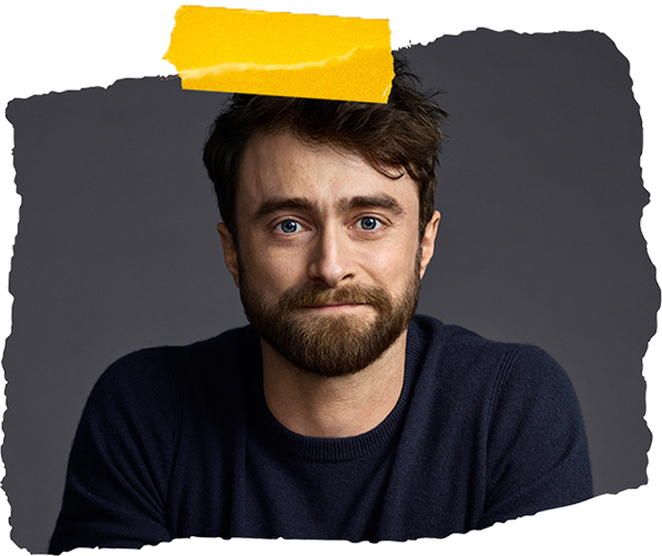 A man with a beard and blue eyes smiles, wearing a dark sweater against a grey background.